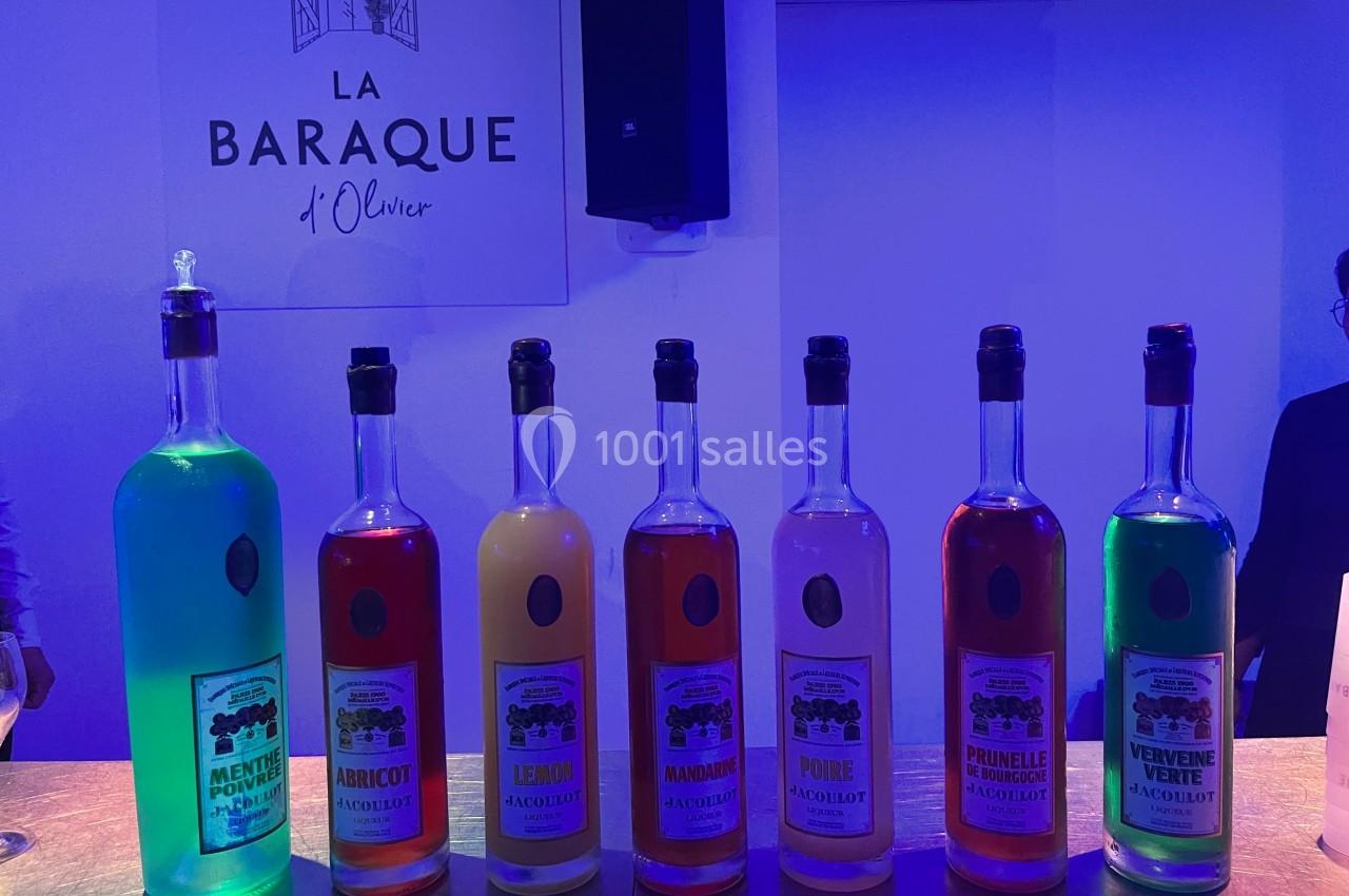 Bouteilles colorées d'apéritifs alignées sur un comptoir, éclairées par une lumière bleutée, avec un panneau en arrière-plan.