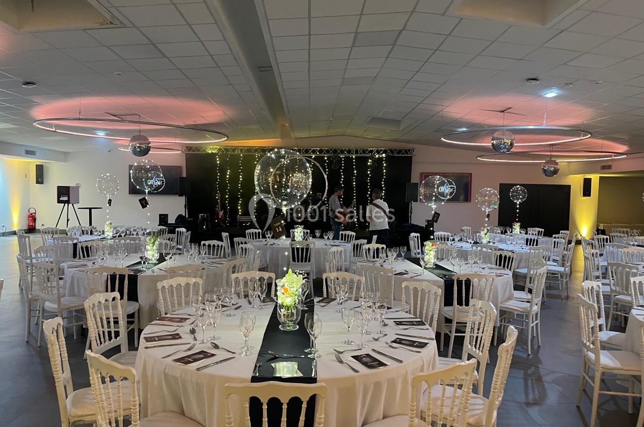 Salle de réception décorée avec des tables rondes, nappes blanches, centres de table lumineux et guirlandes suspendues.