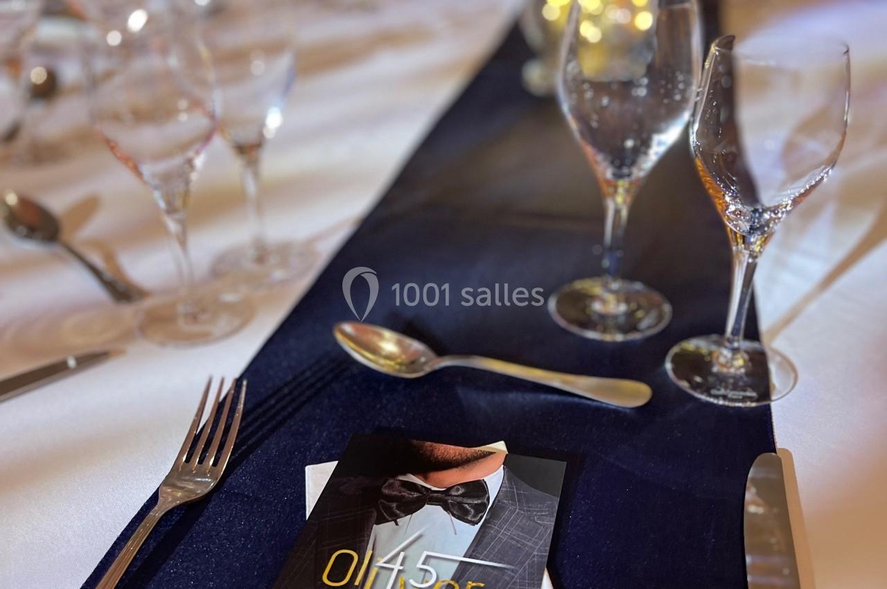 Table élégamment dressée avec nappe bleue, verres, couverts et un menu posé sur une serviette blanche.