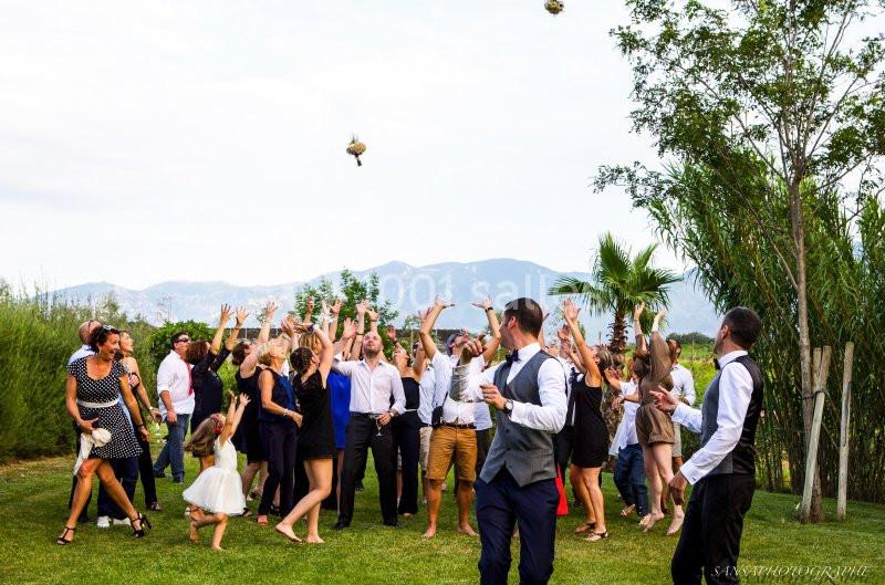 Un groupe de personnes en plein air lève les bras pour attraper un bouquet lancé lors d'une célébration.