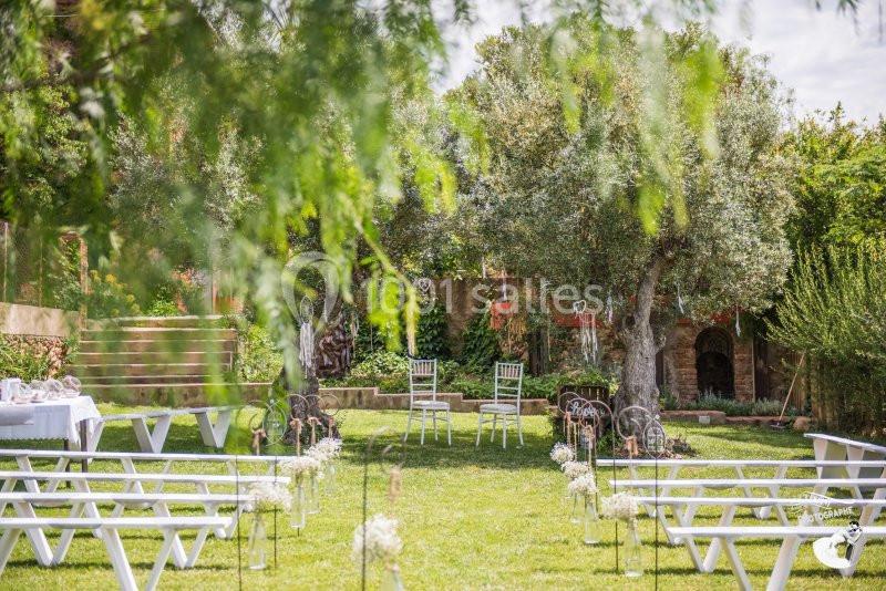 Chaises blanches disposées en extérieur pour une cérémonie, entourées de verdure et de décorations florales.