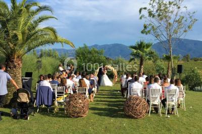 Un artiste chante sur scène avec une personne en costume étincelant sous des lumières violettes, devant un public assis.