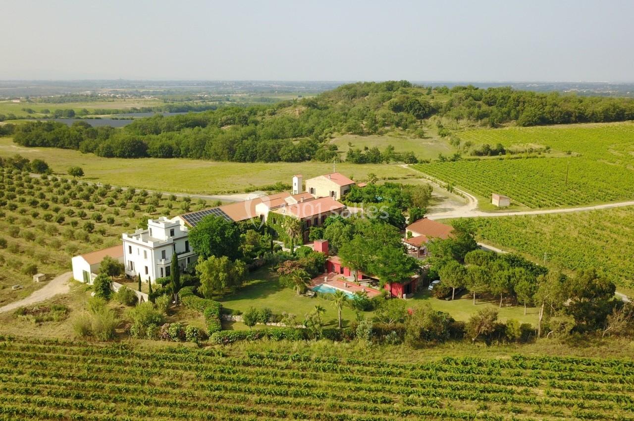 Vue aérienne d'un domaine entouré de vignes et de collines verdoyantes, avec une piscine et plusieurs bâtiments.