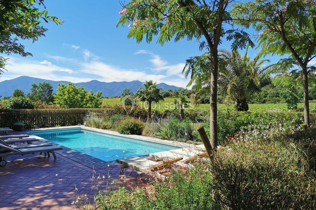 Piscine extérieure entourée de végétation luxuriante avec vue sur des montagnes sous un ciel bleu clair.
