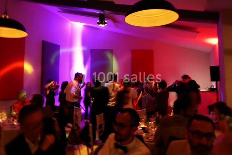 Groupe de personnes dansant et discutant dans une salle éclairée par des lumières colorées.