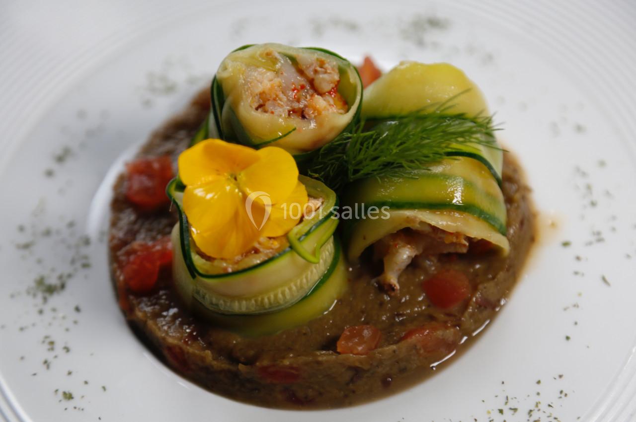Roulés de courgette garnis de fruits de mer sur lit de purée, décorés d'une fleur comestible et d'aneth.