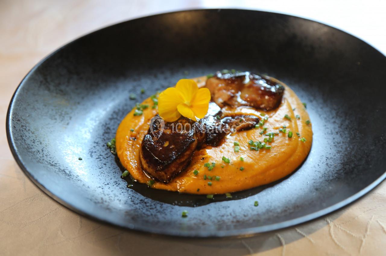 Assiette de purée de légumes orange garnie de morceaux de foie gras poêlé, ciboulette et une fleur comestible.
