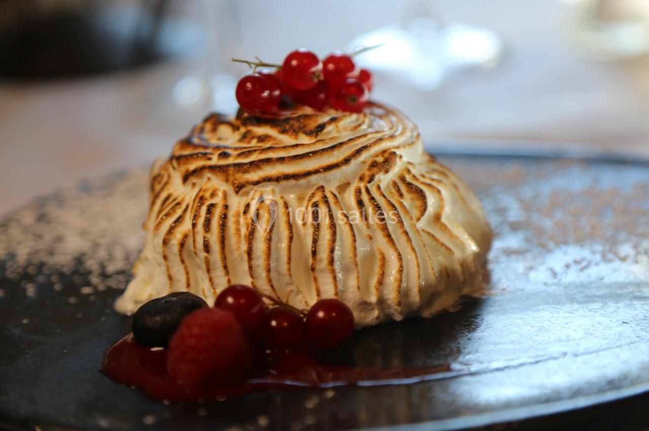 Dessert meringué flambé garni de groseilles rouges, framboise et myrtille, présenté sur une assiette sombre.