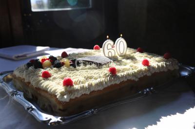 Gâteau rectangulaire décoré de fruits rouges, de crème et de bougies indiquant le chiffre 60, posé sur un plateau argenté.