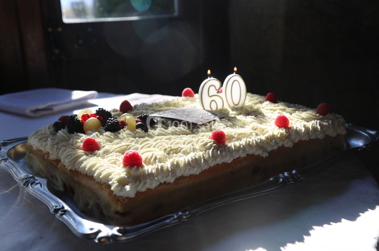 Gâteau rectangulaire décoré de fruits rouges, de crème et de bougies indiquant le chiffre 60, posé sur un plateau argenté.