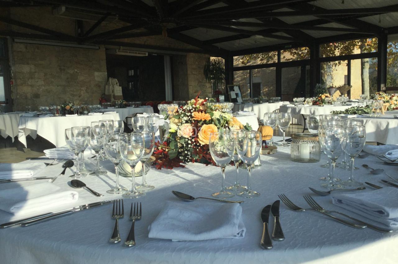 Salle de réception décorée avec des tables dressées, nappes blanches, verres, couverts et centre de table floral.