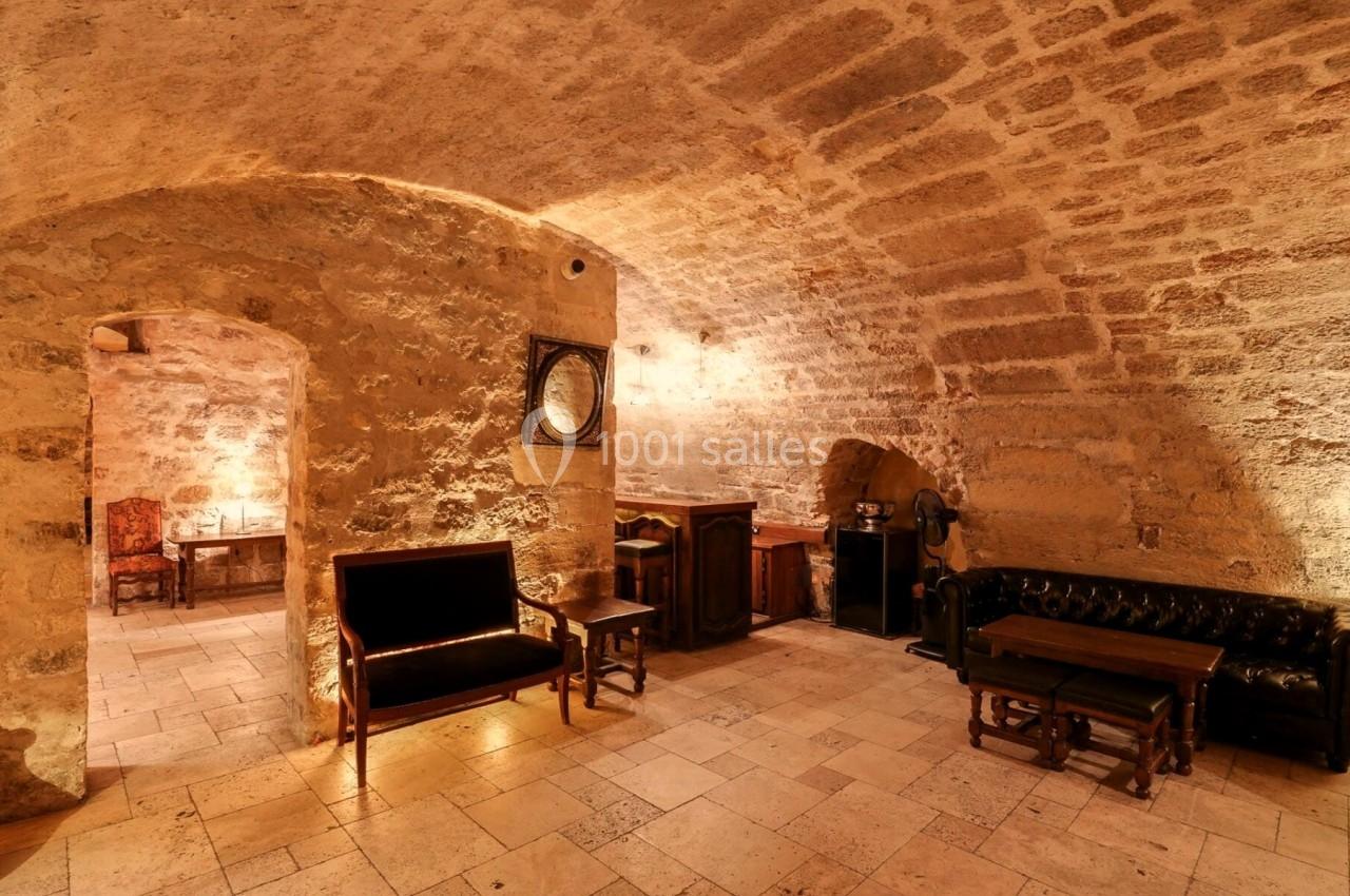 Salle voûtée en pierre avec mobilier en bois et cuir, éclairée par une lumière douce et chaleureuse.