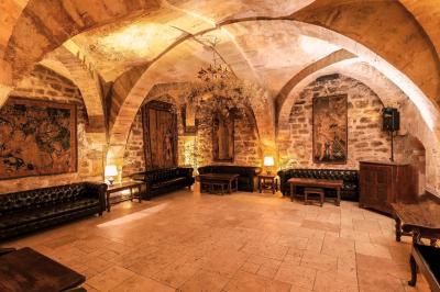 Salle voûtée en pierre éclairée par des lampes et un lustre, avec une table dressée pour un repas.
