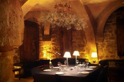 Salle voûtée en pierre éclairée par des lampes et un lustre, avec une table dressée pour un repas.