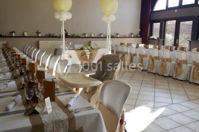 Jardin ensoleillé avec des palmiers au premier plan, pelouse verte et tables hautes recouvertes de nappes noires en arrière…