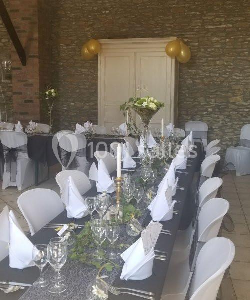 Salle décorée pour un événement, avec tables dressées, nappes noires, serviettes blanches et bougies, devant un mur en…