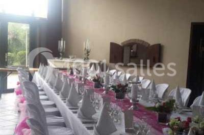 Jardin ensoleillé avec des palmiers au premier plan, pelouse verte et tables hautes recouvertes de nappes noires en arrière…