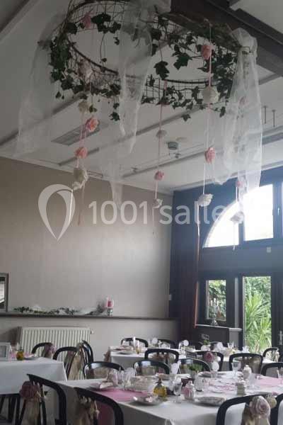 Décoration de salle avec des tables dressées et un lustre orné de fleurs, de lierre et de voilages suspendus.