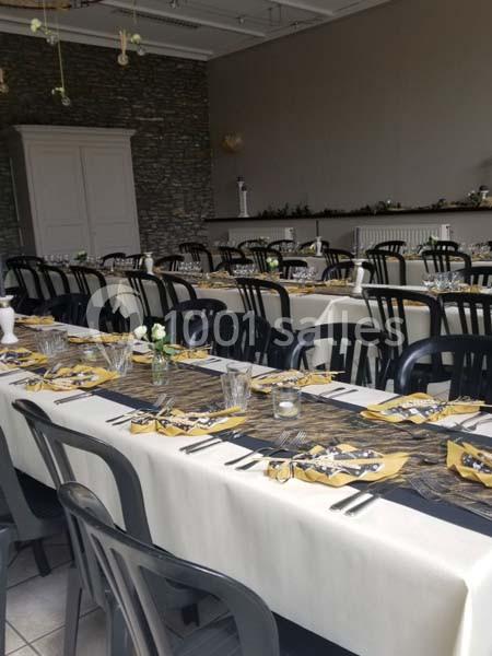 Salle de réception avec tables dressées, nappes blanches, chemins de table noirs et jaunes, et chaises noires.