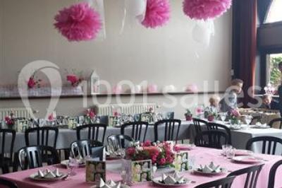 Jardin ensoleillé avec des palmiers au premier plan, pelouse verte et tables hautes recouvertes de nappes noires en arrière…