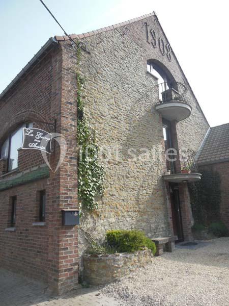 Façade en briques et pierres d'une maison ancienne avec balcon en fer forgé et enseigne murale.