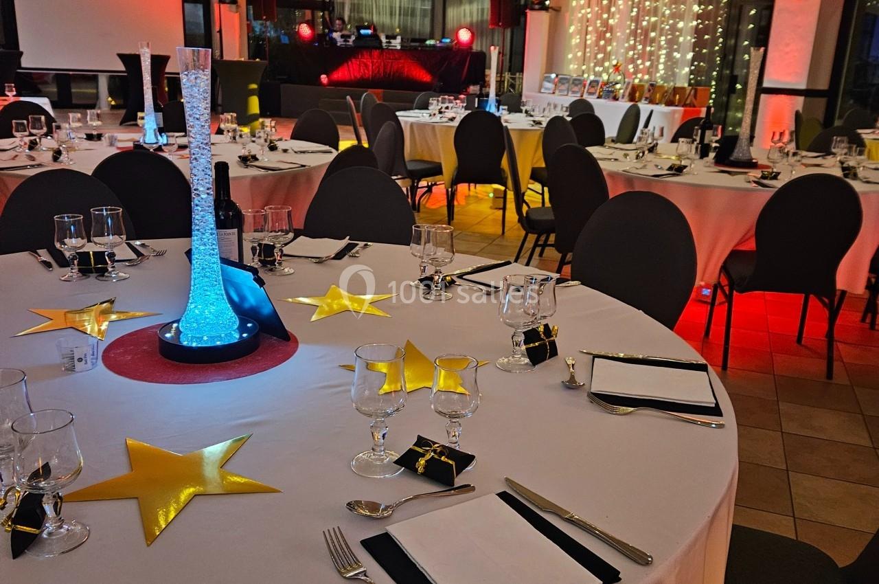 Salle de réception décorée avec des tables rondes dressées, un éclairage chaleureux et des guirlandes lumineuses suspendues.