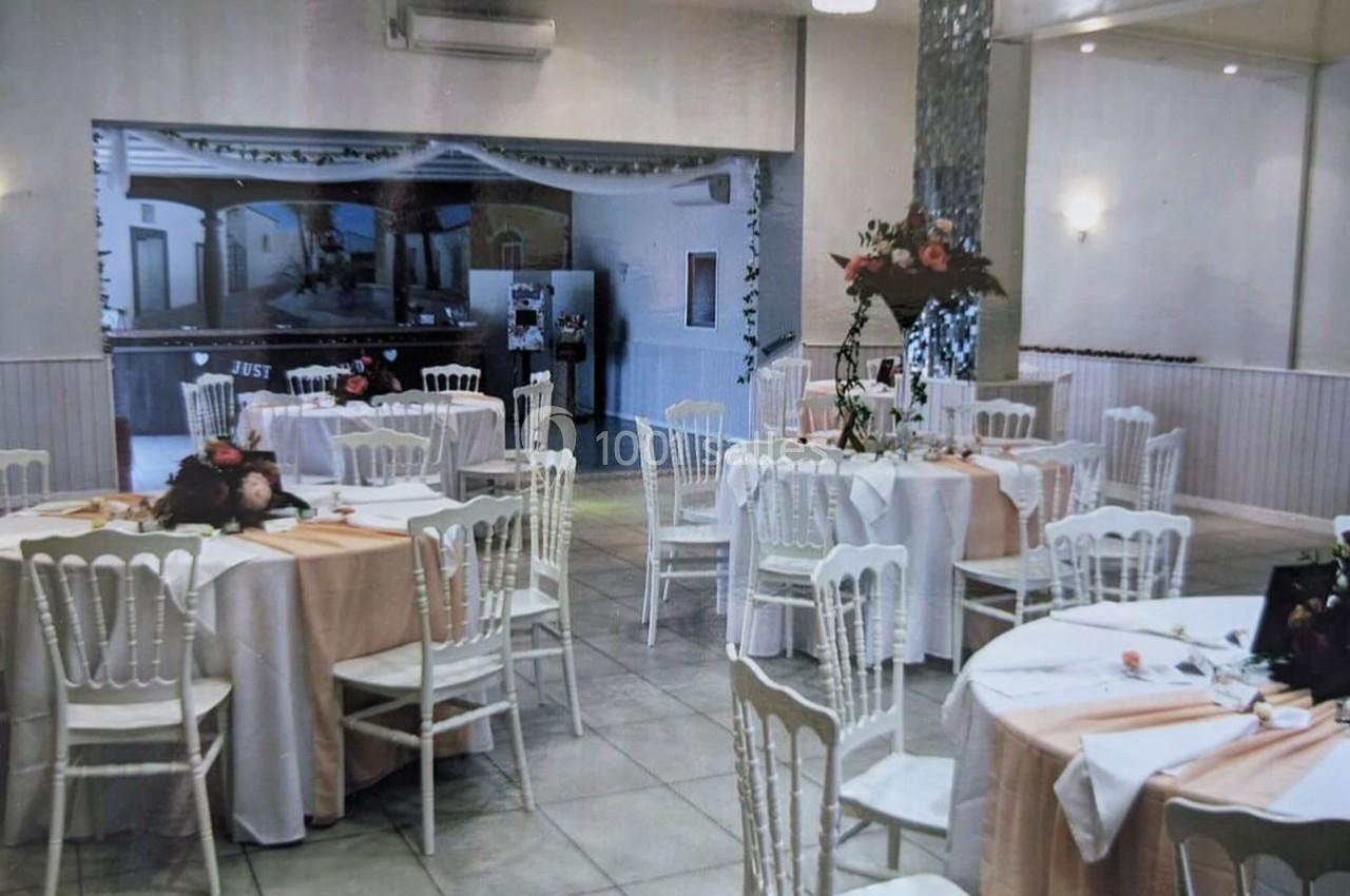 Salle de réception décorée avec des tables rondes, nappes blanches et roses, et des compositions florales.