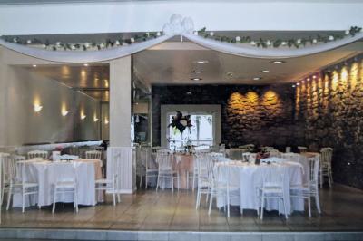 Terrasse en bois avec tables et chaises sous un parasol en chaume, entourée de végétation et de fleurs colorées.
