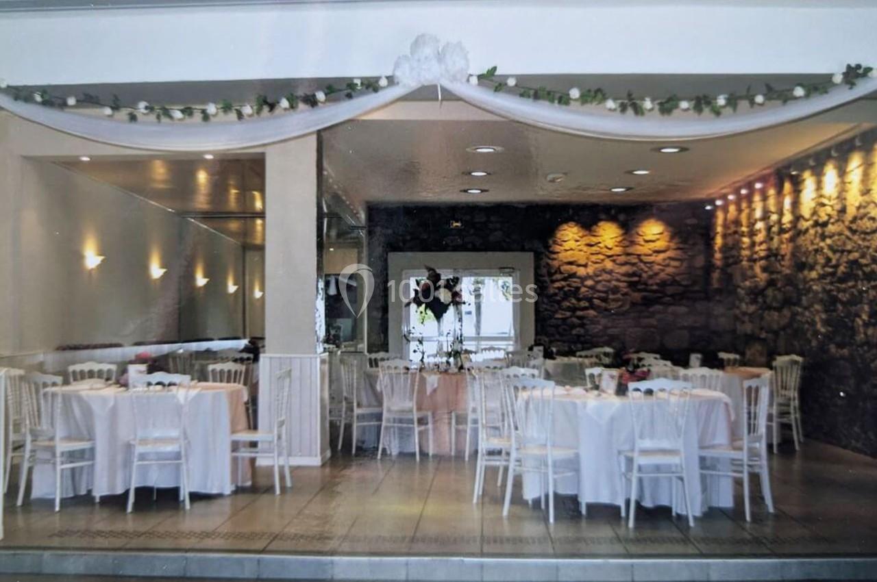 Salle de réception décorée avec des tables rondes, nappes blanches, chaises assorties et guirlande florale suspendue.