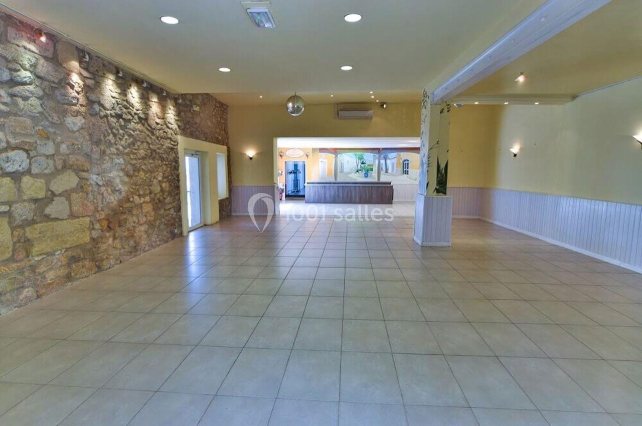 Salle spacieuse avec murs en pierre et carrelage clair, éclairée par des appliques murales et une lumière naturelle.