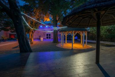 Terrasse en bois avec tables et chaises sous un parasol en chaume, entourée de végétation et de fleurs colorées.