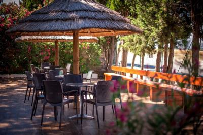 Terrasse en bois avec tables et chaises sous un parasol en chaume, entourée de végétation et de fleurs colorées.