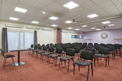 Salle de réunion avec tables rondes dressées de nappes blanches, chaises noires et fournitures de bureau.