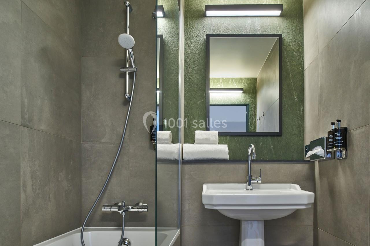 Salle de bain moderne avec douche, baignoire, lavabo blanc, miroir encadré et murs en carrelage gris et vert.