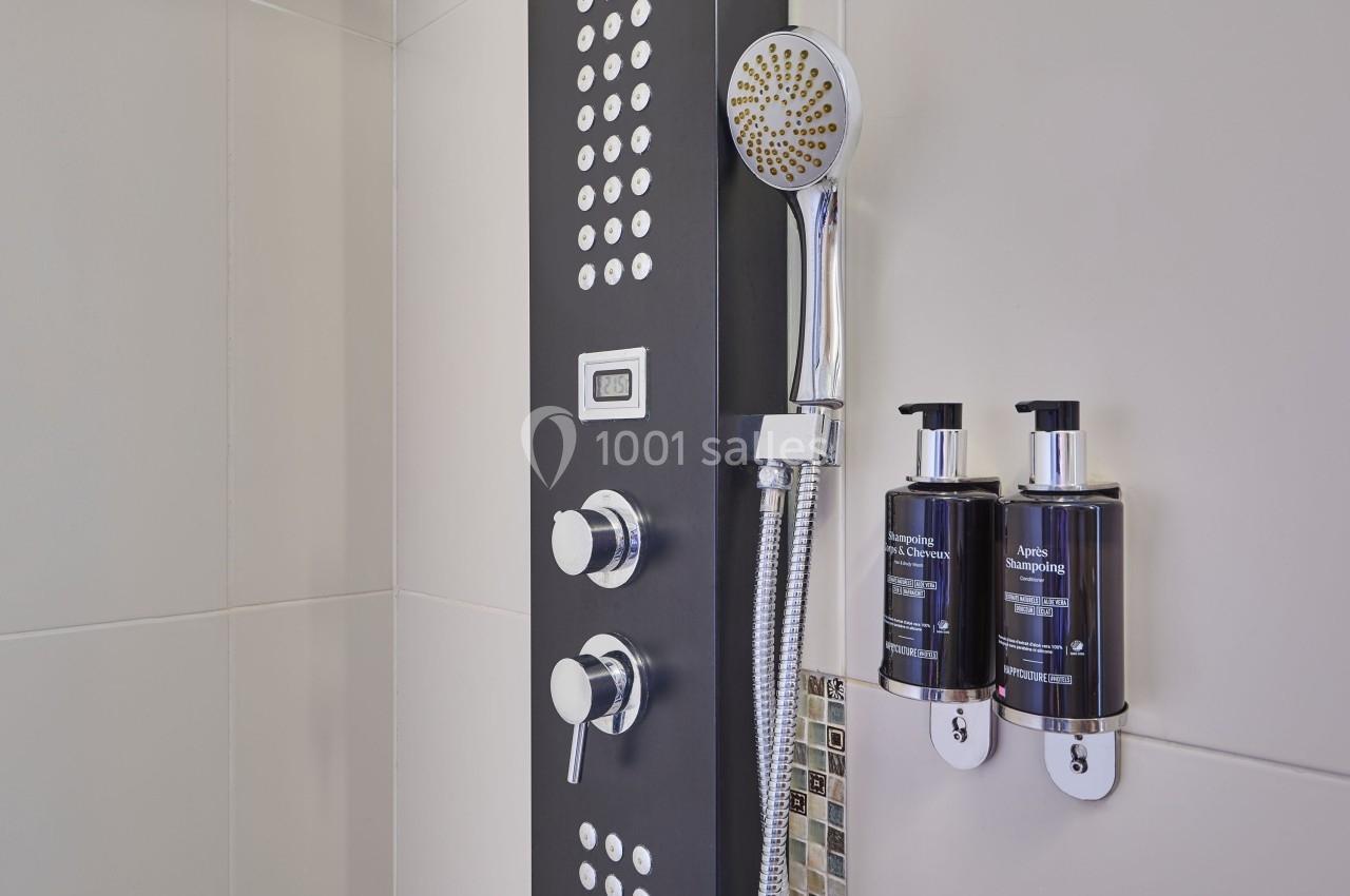 Panneau de douche noir avec pommeau, commandes chromées et distributeurs de savon fixés au mur.