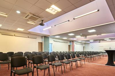 Salle de réunion avec tables rondes dressées de nappes blanches, chaises noires et fournitures de bureau.