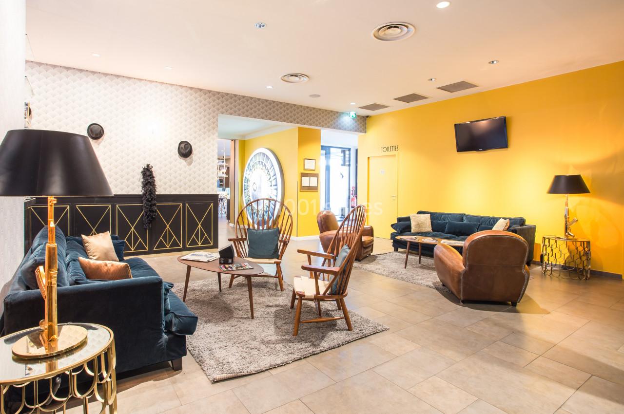 Salon lumineux avec murs jaunes, mobilier vintage, canapés en velours, fauteuils en bois et décoration élégante.