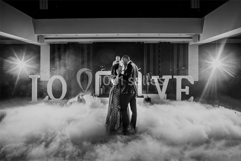 Un couple danse au milieu d'une piste entourée de fumée, avec des lettres géantes formant ’LOVE’ en arrière-plan.