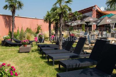 Salle de restaurant lumineuse avec grandes baies vitrées, tables dressées et vue sur une terrasse extérieure.