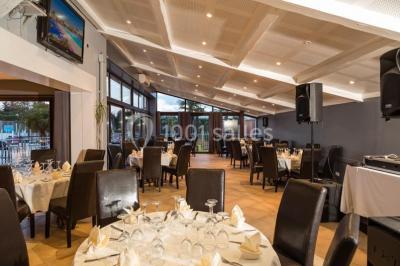 Salle de restaurant lumineuse avec grandes baies vitrées, tables dressées et vue sur une terrasse extérieure.