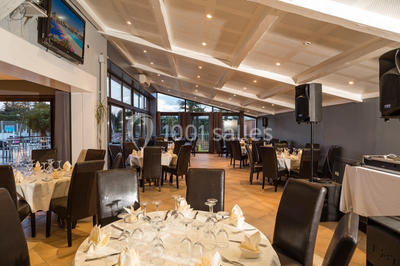 Salle de restaurant lumineuse avec tables dressées, chaises en cuir noir et grandes baies vitrées donnant sur l'extérieur.