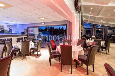 Salle de restaurant lumineuse avec grandes baies vitrées, tables dressées et vue sur une terrasse extérieure.