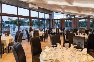 Salle de restaurant lumineuse avec grandes baies vitrées, tables dressées et vue sur une terrasse extérieure.