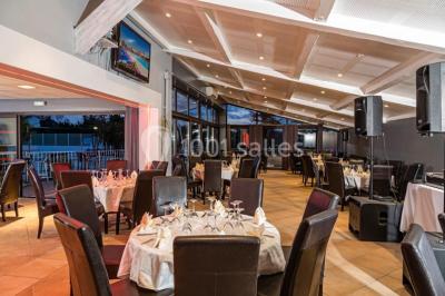 Salle de restaurant lumineuse avec grandes baies vitrées, tables dressées et vue sur une terrasse extérieure.