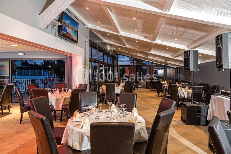 Salle de restaurant lumineuse avec tables dressées, chaises en cuir sombre et grandes baies vitrées donnant sur l'extérieur.