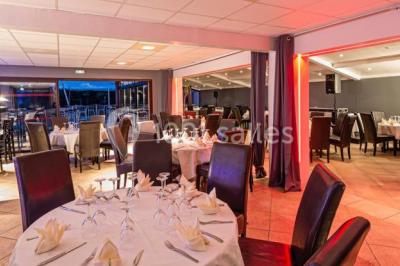 Salle de restaurant lumineuse avec grandes baies vitrées, tables dressées et vue sur une terrasse extérieure.