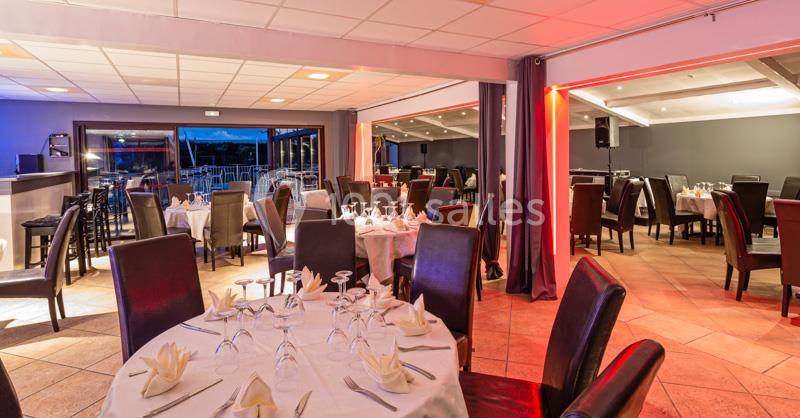 Salle de restaurant lumineuse avec tables dressées, chaises en cuir sombre et grandes baies vitrées donnant sur l'extérieur.