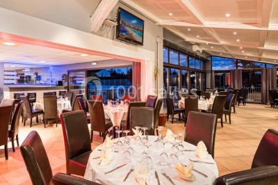 Salle de restaurant lumineuse avec grandes baies vitrées, tables dressées et vue sur une terrasse extérieure.