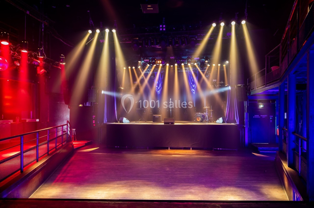 Salle de concert vide avec scène éclairée par des projecteurs colorés et balustrades sur les côtés.