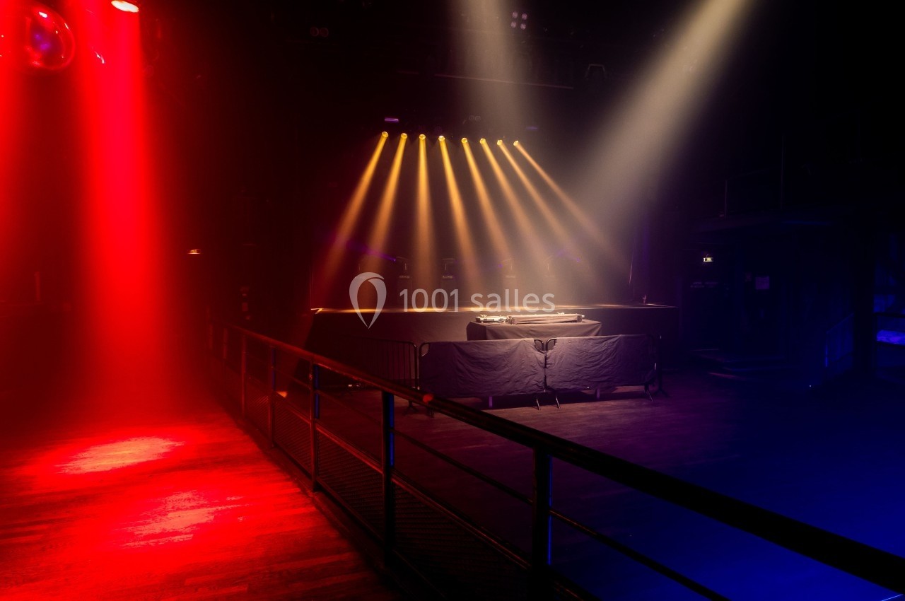 Scène de concert vide éclairée par des projecteurs rouges et jaunes dans une salle sombre.